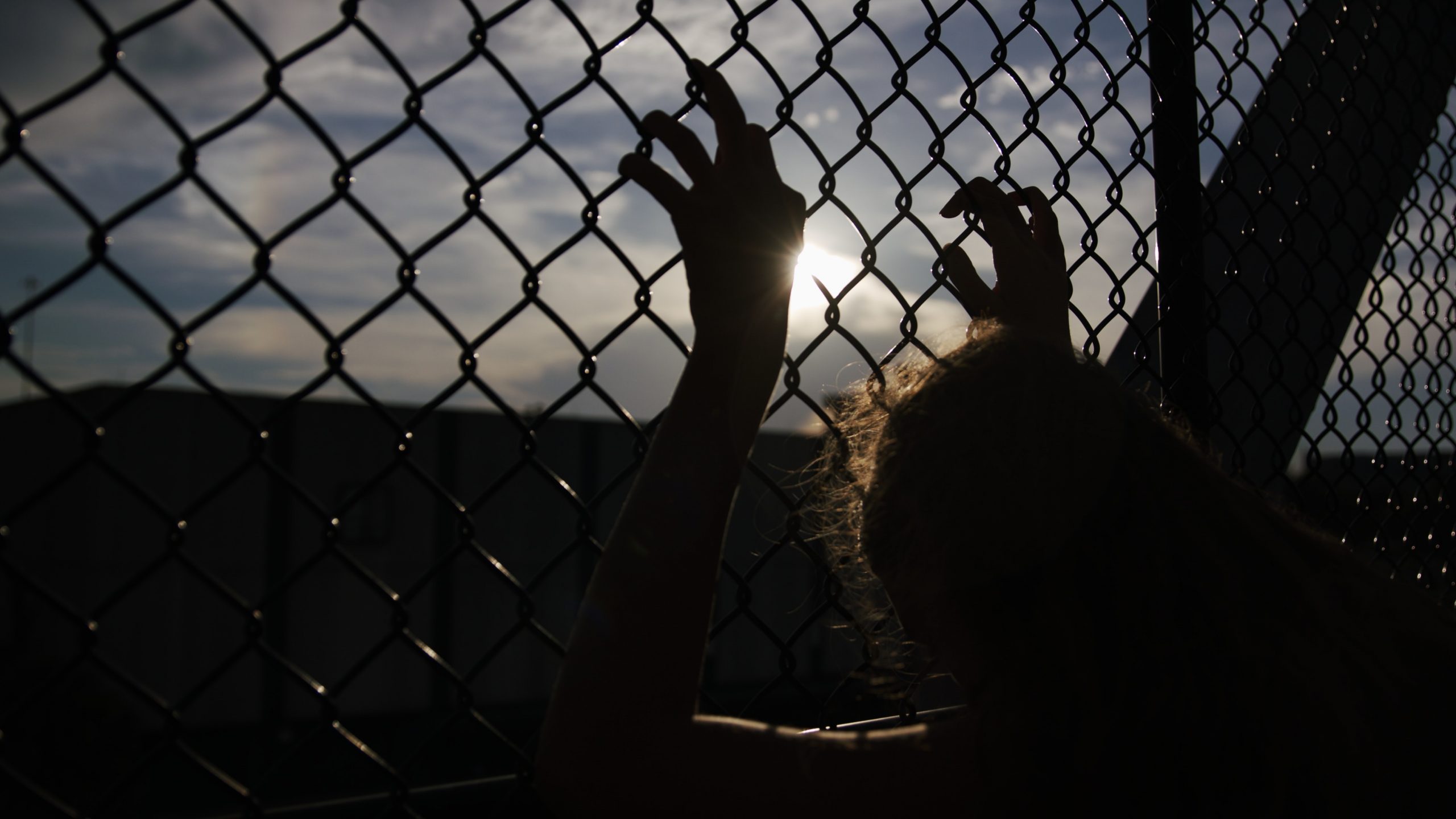 Image of a person holding on chain link fence.