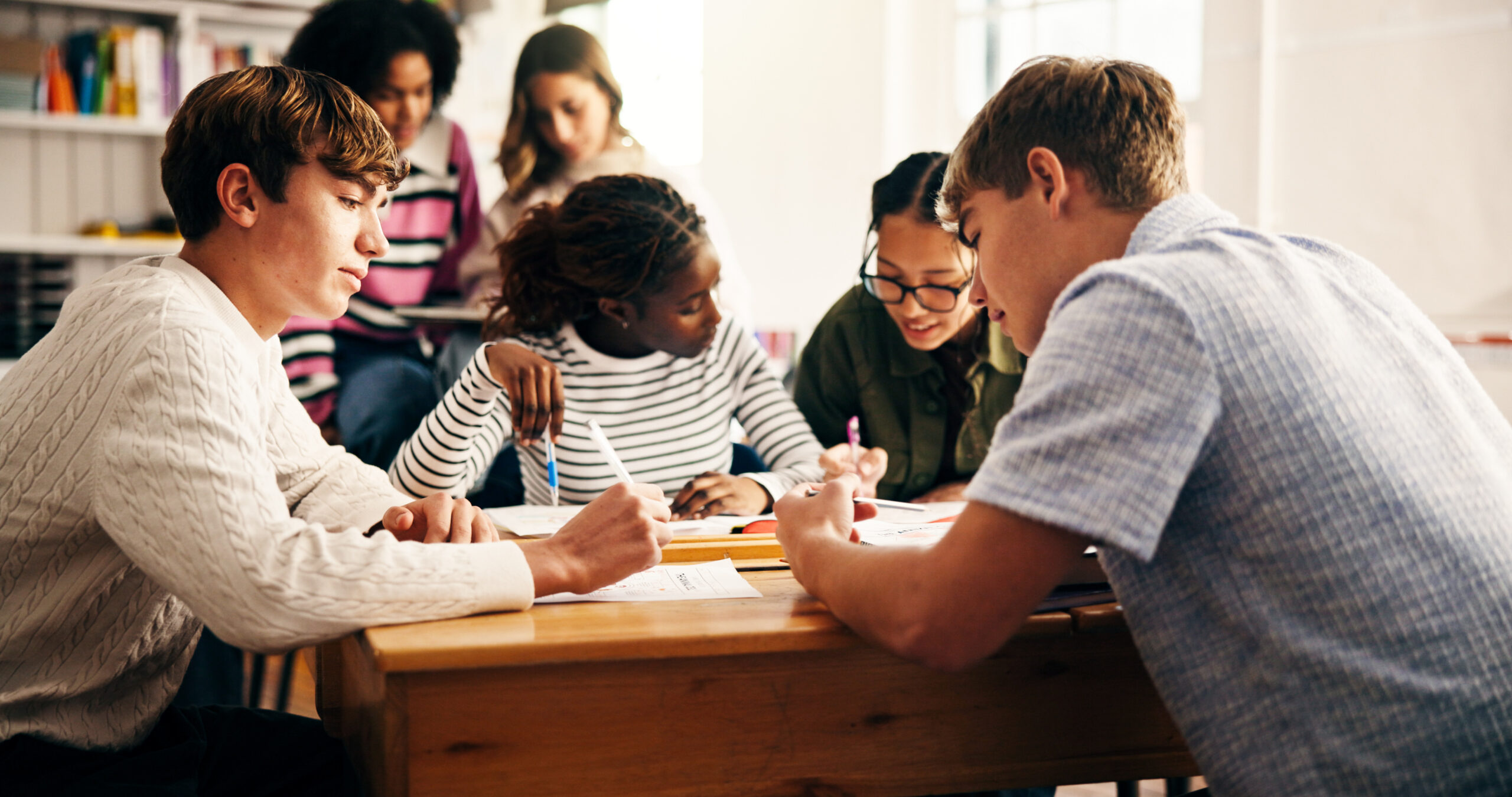 A group of middle school students gathered around a desk, working together on an assignment.
