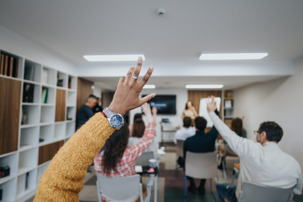 From the back of the room, we see a group of adult professionals raising their hands during a training.