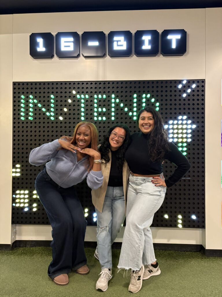 The Rooted Collective team posing in front of a digital sign that says In/Tend.