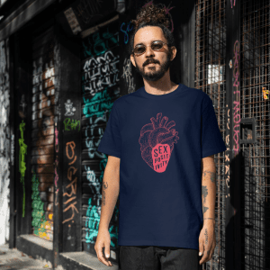Man with dark hair pulled back and a beard, wearing sunglasses and a navy blue t-shirt with a pink anatomically correct heart with the words sex positivity written in the bottom.