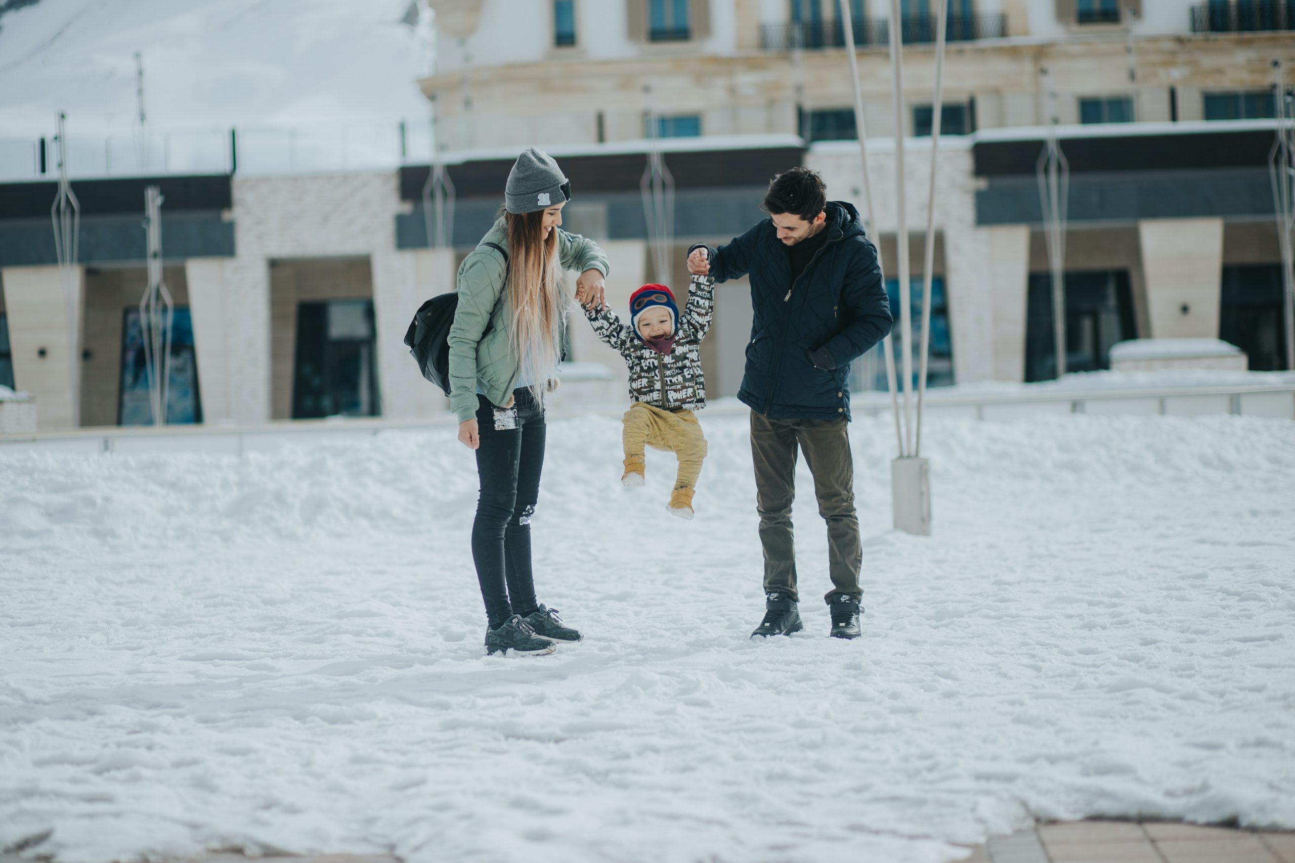 Young mom and dad hold toddler between their arms in a snowy park