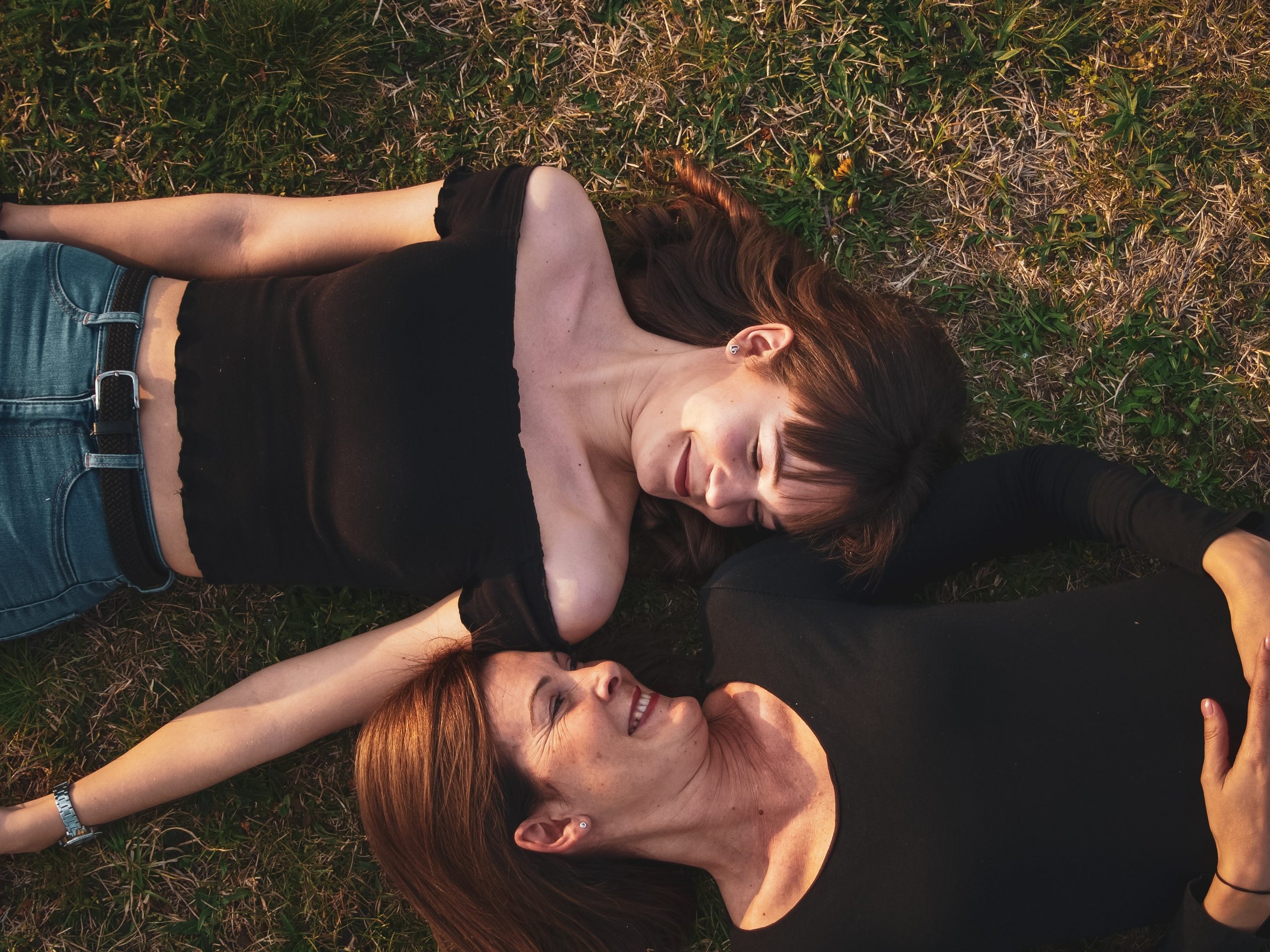 Image of mother and daughter laying with their heads together in a field