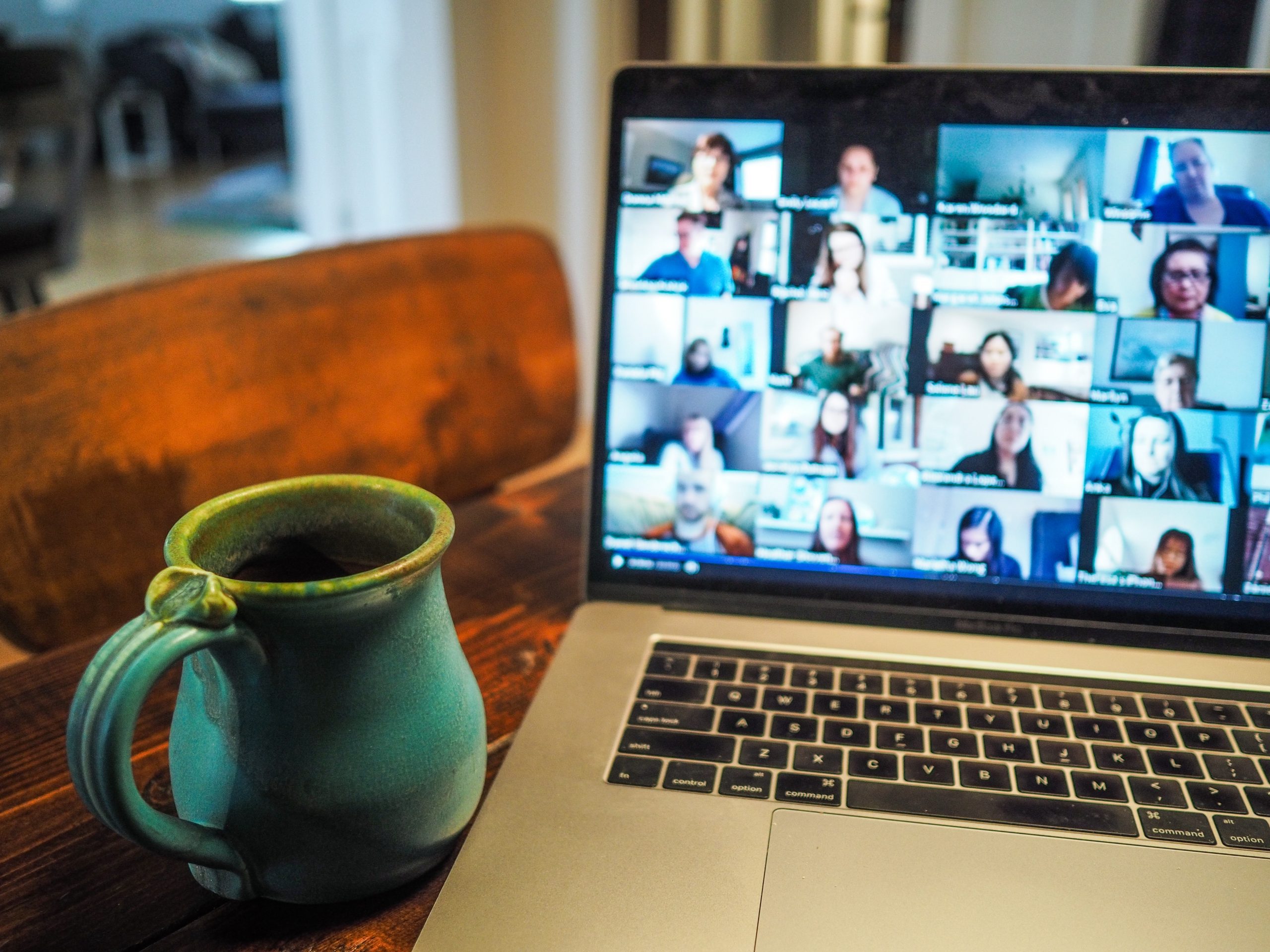 laptop with a zoom call next to a teal coffee mug on a wooden table