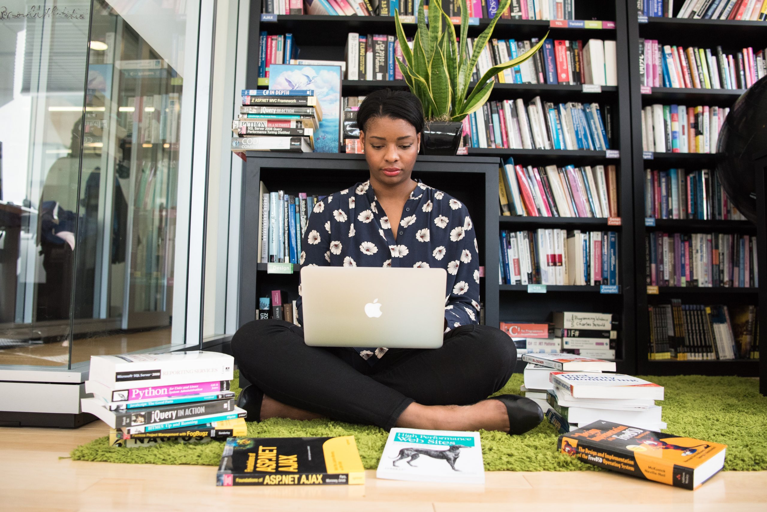 woman sitting on the floor surrounded by books using a MacBook