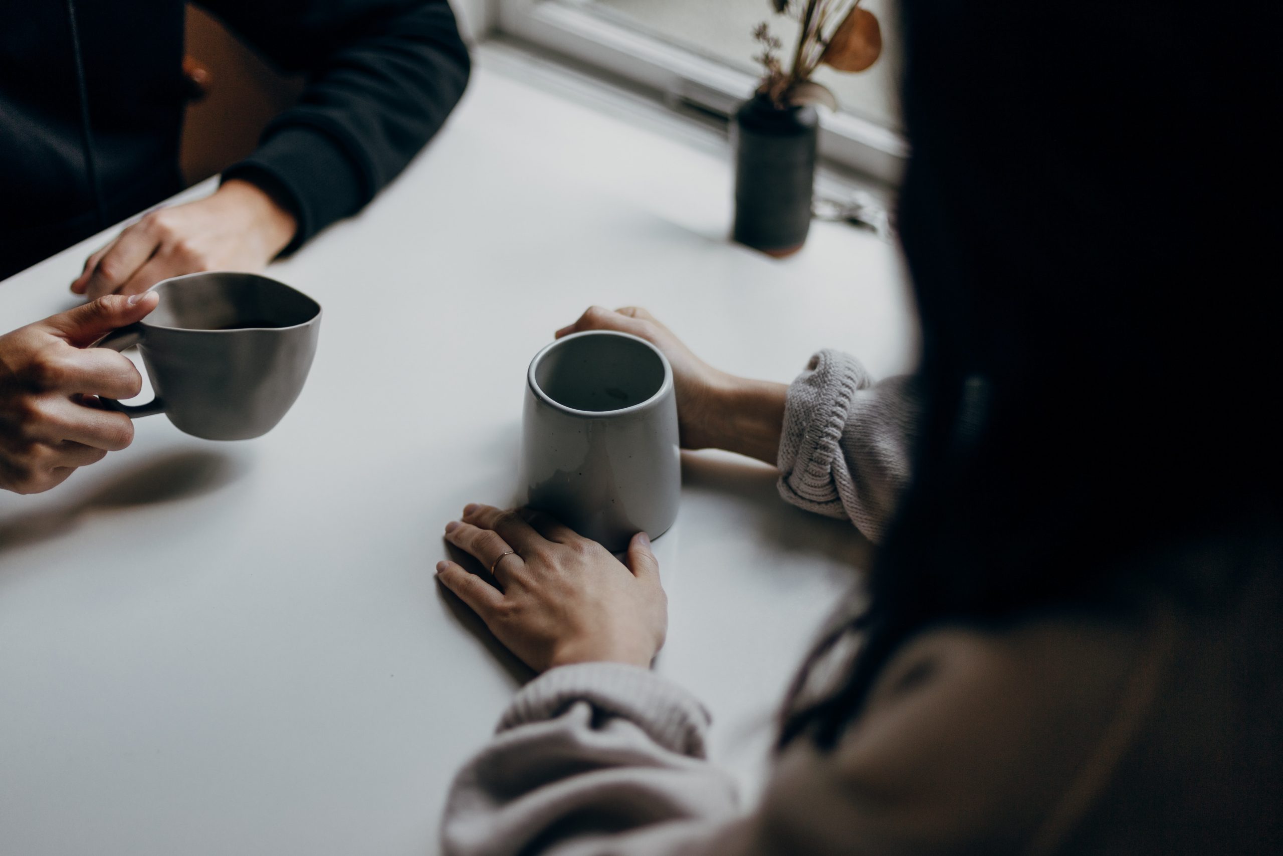 Image of two people sitting across from each other holder coffee mugs.