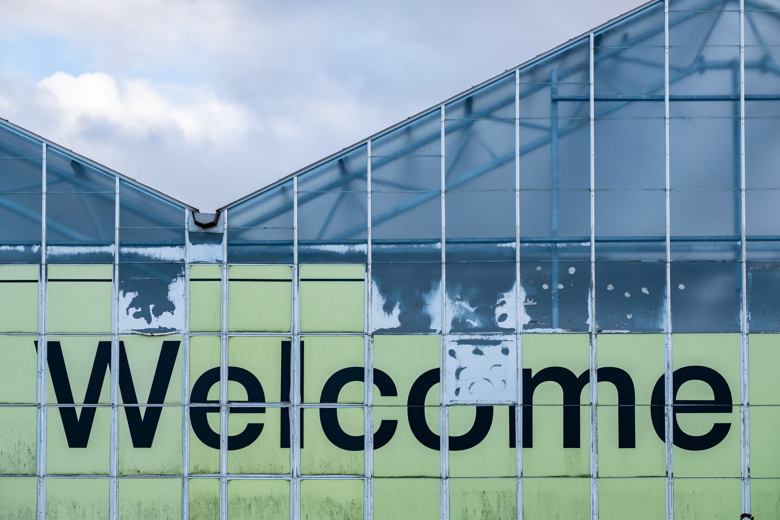 wooden welcome sign in cursive on a fake shrub background