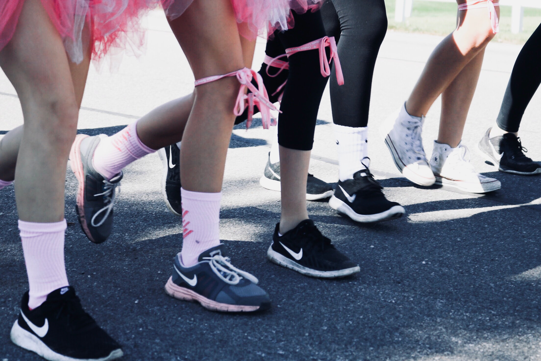 Photo of runners legs at the starting line with some runners having pink ribbons tied across their thighs for breast cancer awareness